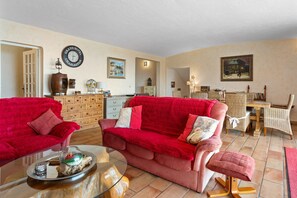 Un salon avec deux canapés rouges, une table basse en verre, un meuble en bois et un coin repas avec des chaises en osier.