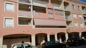 Un edificio de varios pisos con balcones, un acceso cubierto y varios coches aparcados.