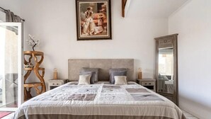 Un dormitorio con una cama grande, una silla de madera, un cuadro en la pared y un espejo.