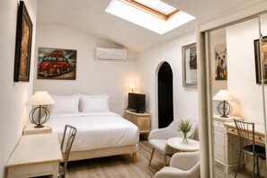 A hotel room with a bed, a desk, a chair, a TV, and a skylight.