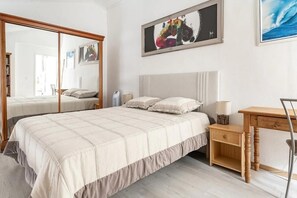 Et soveværelse med seng, sengebord, lampe og et spejl.