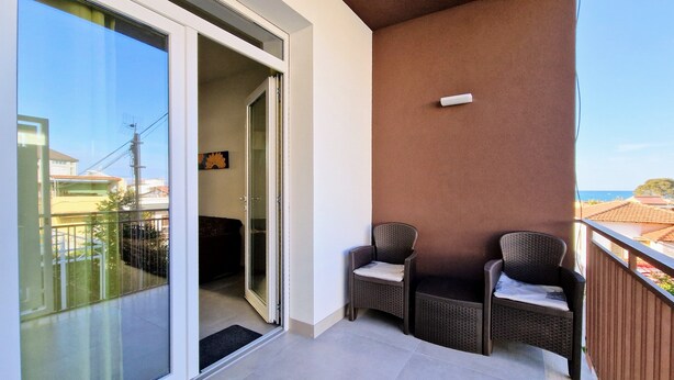 A balcony with two wicker chairs, a glass door leading to an interior room, and a view of buildings and the sea. - Apartment 'Appartamento Della Luna 2' with Sea View, Balcony and Wi-Fi (Alcamo)