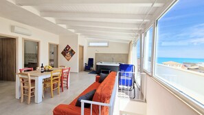 A spacious living area with a dining table, a sofa, and a view of the sea.