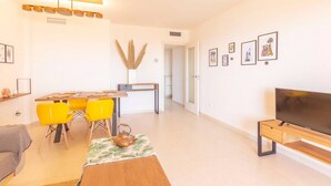 A modern living room with a dining area, a TV, and artwork on the walls. - Apartamento Ambar Beach by Costa CarpeDiem (Calpe)