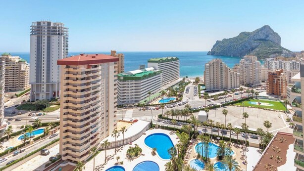 A high-rise hotel with multiple balconies, a swimming pool area, and a view of the sea and a mountain. - Apartamento Ambar Beach by Costa CarpeDiem (Calpe)