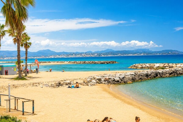 A beach with clear blue water, a rocky breakwater, and palm trees.