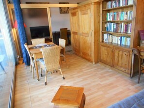 A living room with a wooden dining table, wicker chairs, a bookshelf, and a television.