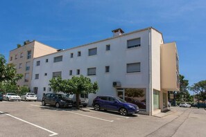 Un edificio de varios pisos con estacionamiento, varios coches aparcados y un árbol al frente.