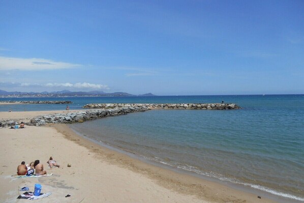 A beach with people sunbathing, a rocky breakwater, and distant mountains.