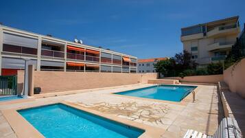 Un espace piscine comprenant deux piscines, un espace détente couvert et un bâtiment doté de balcons.