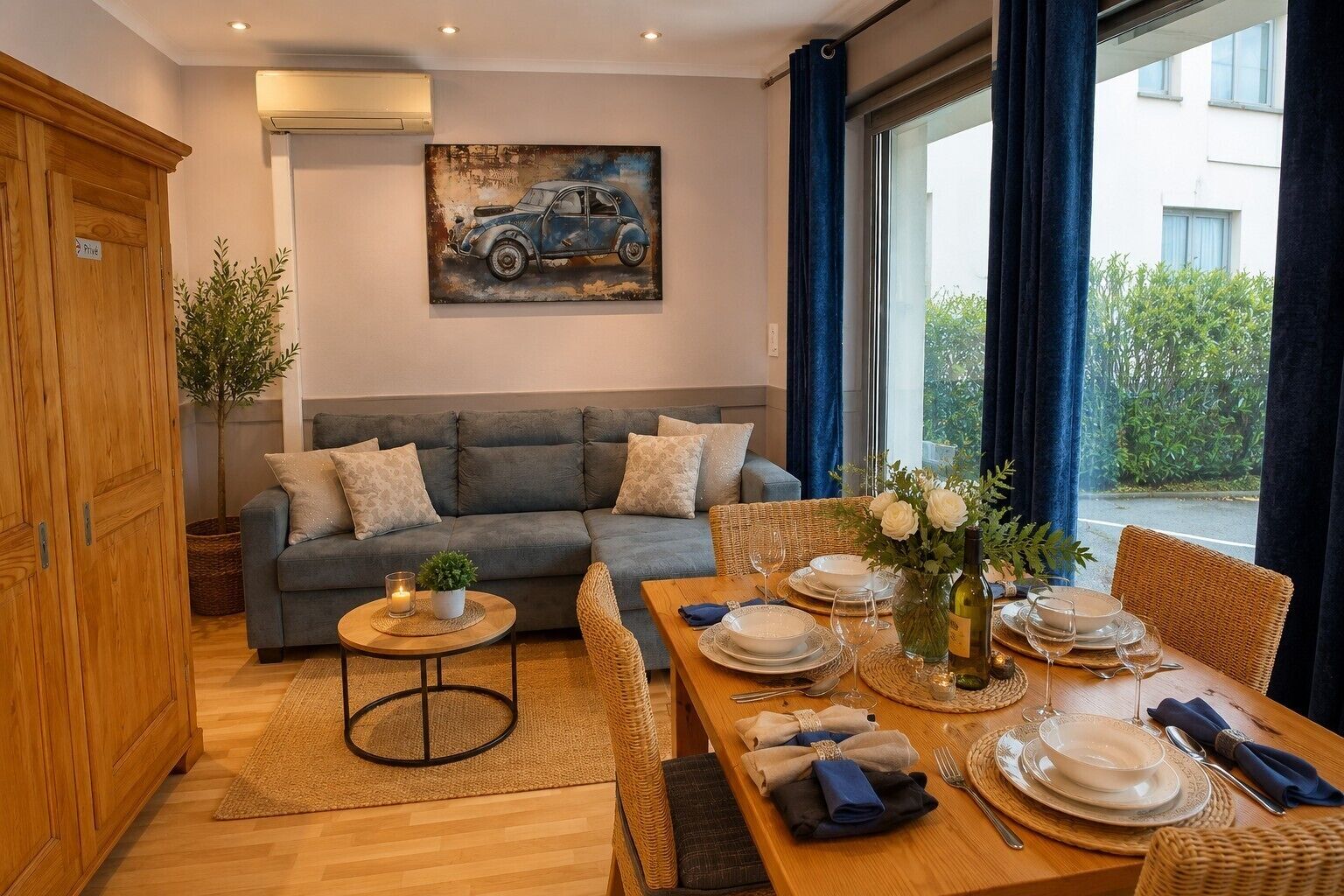 Un salon meublé avec un canapé, une table à manger dressée pour quatre personnes et un tableau accroché au mur.