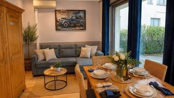 Un salon meublé avec un canapé, une table à manger dressée pour quatre personnes et un tableau accroché au mur.