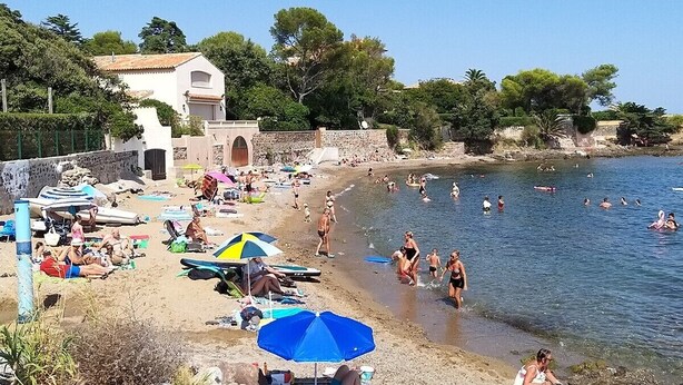 A beach with people swimming and sunbathing, umbrellas, and a building with a stone wall. - Apartment 200 m from Calanques & Sea, Wi-Fi, Air Conditioning, Private Parking (Saint-Aygulf)