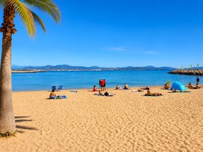 Ein Strand mit badenden Menschen, Palmen und einem strahlend blauen Himmel.