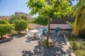 A patio area with a table and chairs, surrounded by greenery and a stone wall.