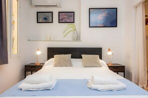 Una habitación de hotel con una cama grande, dos mesitas de noche con lámparas, un cabecero y tres cuadros en la pared.