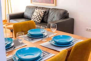 Ein Esstisch ist gedeckt mit blauen Tellern, Gläsern und Besteck. Im Hintergrund sieht man eine Couch und ein Kissen mit Muster.