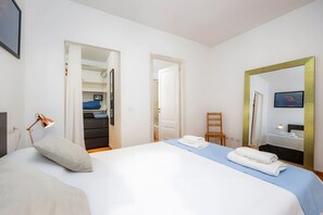 A hotel room with a bed, a desk with a lamp, a chair, a bathroom with a mirror, and a wardrobe.