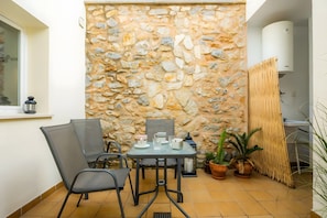 A small outdoor seating area with a stone wall backdrop, a table with chairs, and potted plants.
