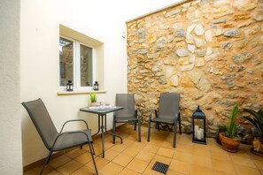 Eine kleine Terrasse mit einer Steinmauer, zwei Stühlen, einem Tisch und einem Fenster.