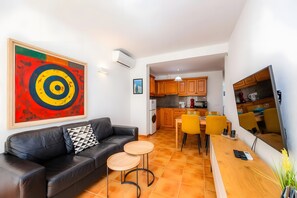 A living room with a black leather sofa, a colorful abstract painting, and a dining area with yellow chairs.