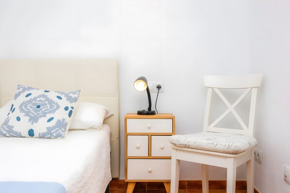A bedroom with a bed, a nightstand with a lamp, and a white chair.