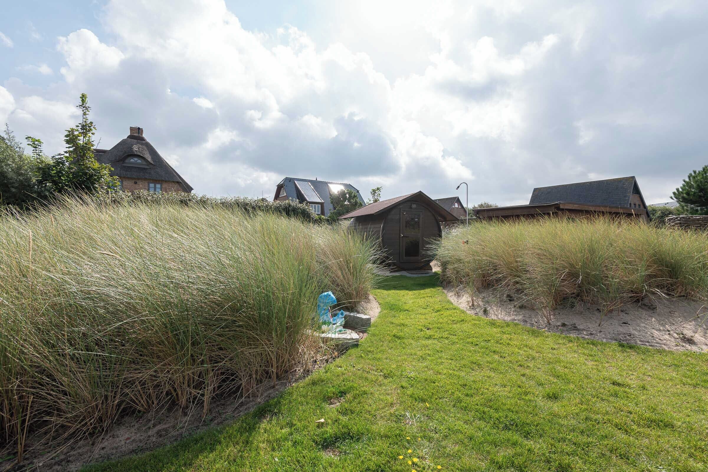 A pathway leading to a traditional thatched-roof house surrounded by tall grasses and a clear sky.