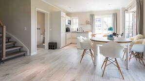 Una cocina moderna con armarios blancos, una zona de comedor con sillas blancas y una escalera.