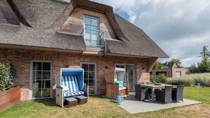 Una casa con techo inclinado, un balcón, un patio con mobiliario exterior y fachada de ladrillo.
