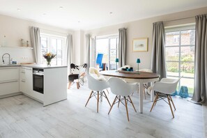Une cuisine moderne avec des meubles blancs, un four encastré et un coin repas comprenant une table ronde et des chaises blanches.