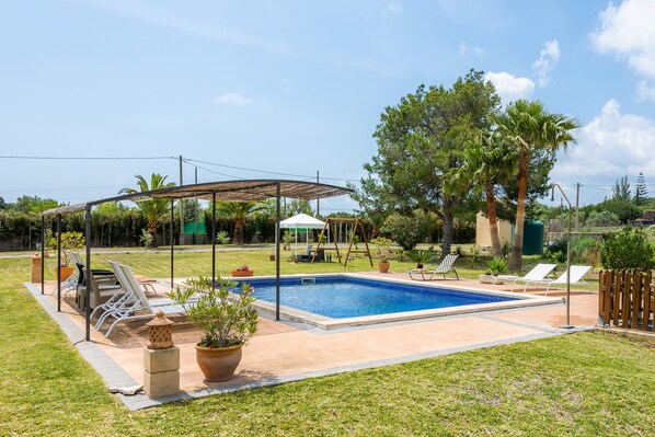 A backyard with a swimming pool, lounge chairs, a pergola, and a children's play area.