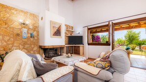 Una sala de estar con pared de piedra, chimenea, televisor y vistas al exterior.
