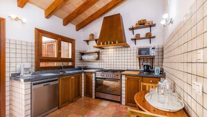 Una cocina compacta equipada con lavavajillas, estufa, horno y microondas. Cuenta con armarios de madera, salpicadero de azulejos y techo de madera.