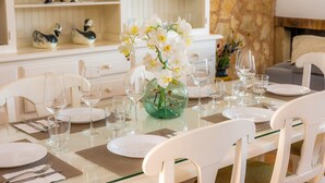 Una mesa de comedor dispuesta con platos blancos, vasos y un jarrón verde con flores blancas.