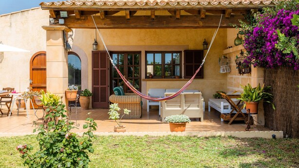 Una casa con patio, mobiliario exterior y una hamaca.