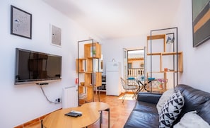 Una sala de estar moderna con un televisor de pantalla plana, una mesa de centro de madera, un sofá de cuero negro y una zona de comedor con una mesa y sillas.