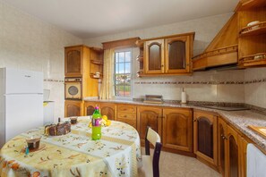 Eine Küche mit Holzausstattung, einem Fenster, einem Tisch mit Blumenmuster und einem Kühlschrank.