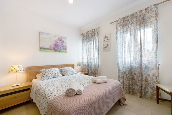 A bedroom with a bed, nightstand, and a painting on the wall.