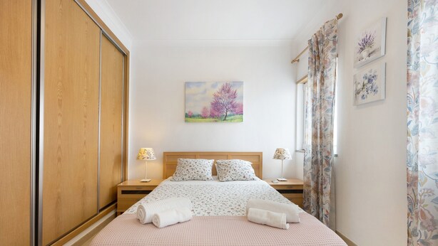 Ein Schlafzimmer mit einem Bett, einem Schrank aus Holz, Nachttischen, Lampen und einem Bild an der Wand.