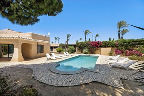 A pool area with lounge chairs, a swimming pool, and surrounding greenery.