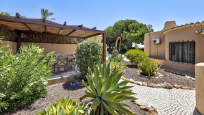 Un patio con una pérgola, zona de estar y diversas plantas.