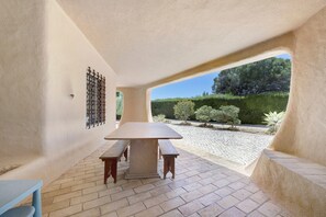 A patio area with a table and benches, a view of a landscaped garden, and a stone floor.