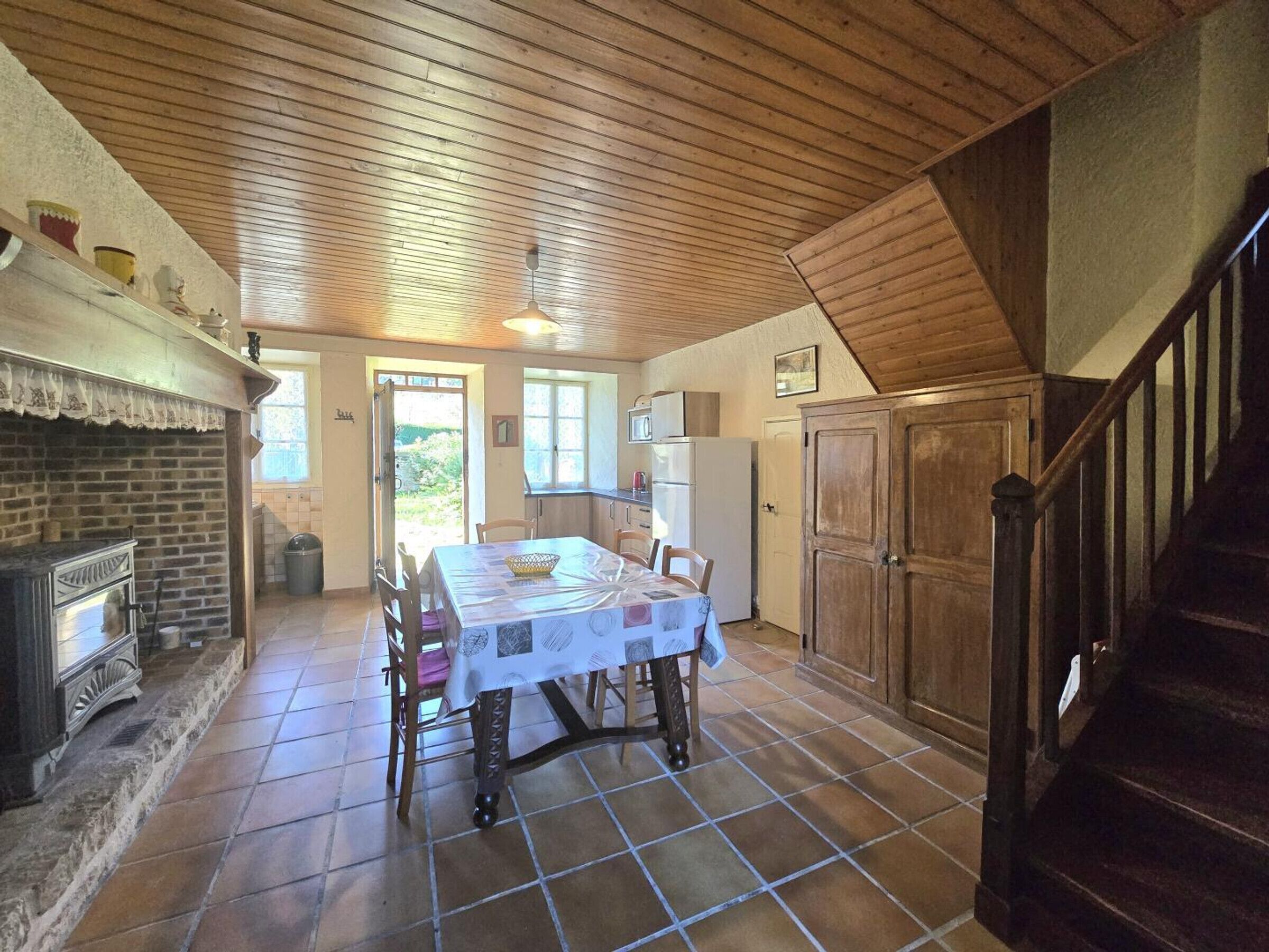 A rustic kitchen with a tiled floor, wooden ceiling, and a dining table set for four.