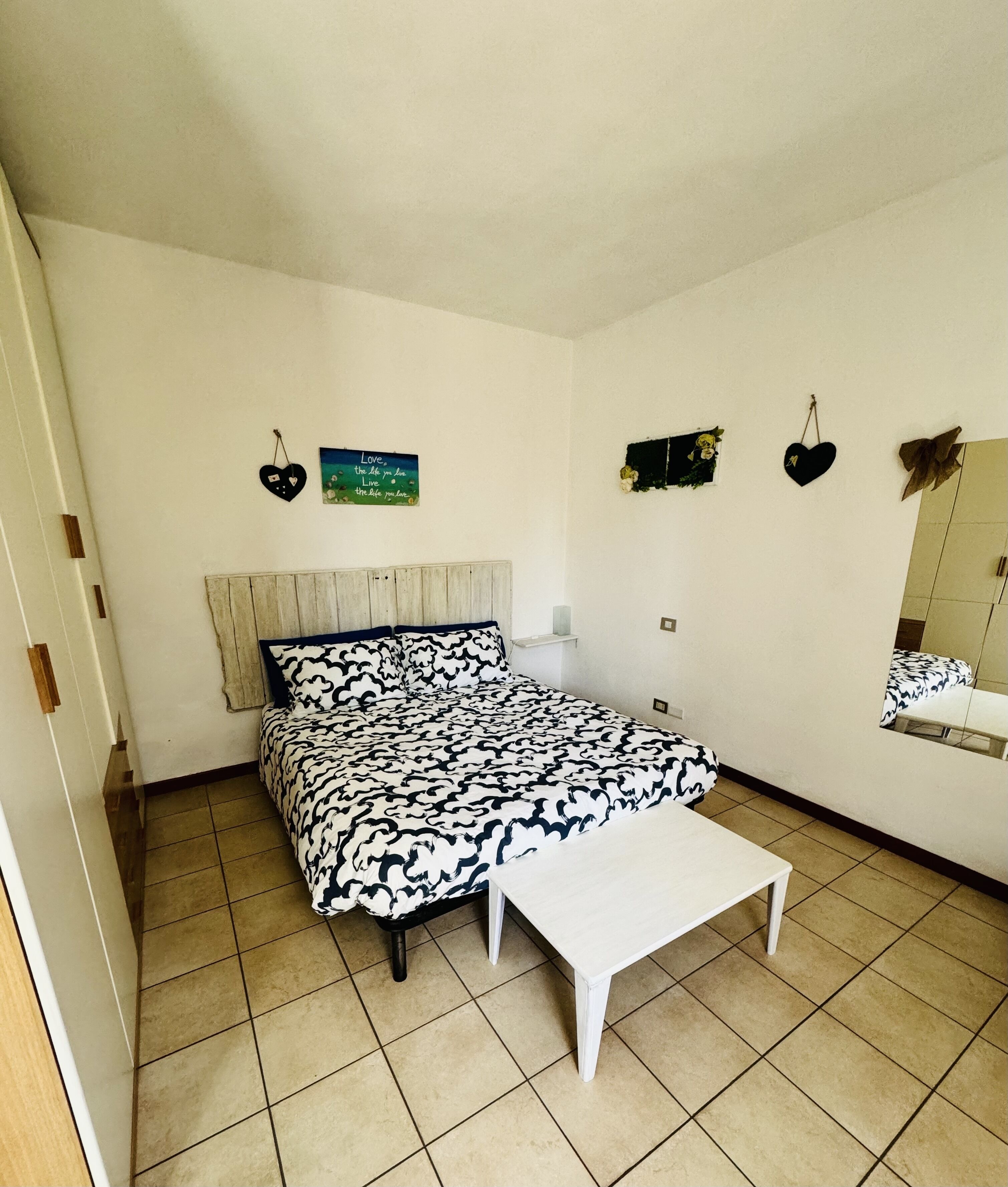 Ein Schlafzimmer mit einem Bett, einem Nachttisch, einem kleinen Tisch und einem Spiegel an der Wand.