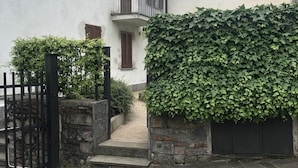 Un bâtiment dont l’entrée est pavée de pierres, qui possède une allée bordée de grilles et un grand mur recouvert de lierre.