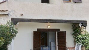 Un edificio con un alero de madera, una puerta con contraventanas abiertas y un ventanal con contraventanas.