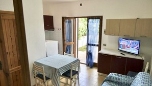 Una habitación compacta con una mesa de comedor, sillas, un sofá, un televisor y una zona de cocina.