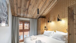 A bedroom with a large bed, wooden ceiling, and a window with curtains. - New apartment in Méribel with sauna and parking (Méribel)