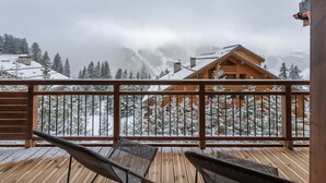 A wooden deck with a view of a snow-covered mountain and a wooden cabin. - New apartment in Méribel with sauna and parking (Méribel)