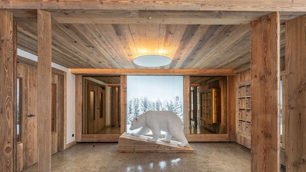 A spacious hallway with wooden walls and a polished floor, leading to a room with a large window and a polar bear sculpture. - New apartment in Méribel with sauna and parking (Méribel)